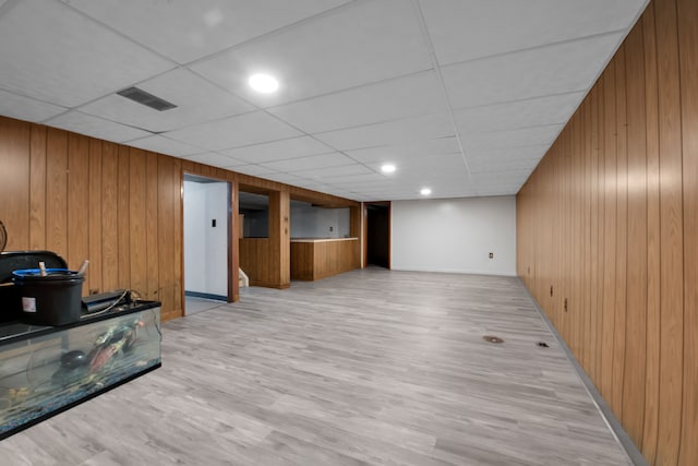 basement featuring a paneled ceiling, wooden walls, and light hardwood / wood-style flooring