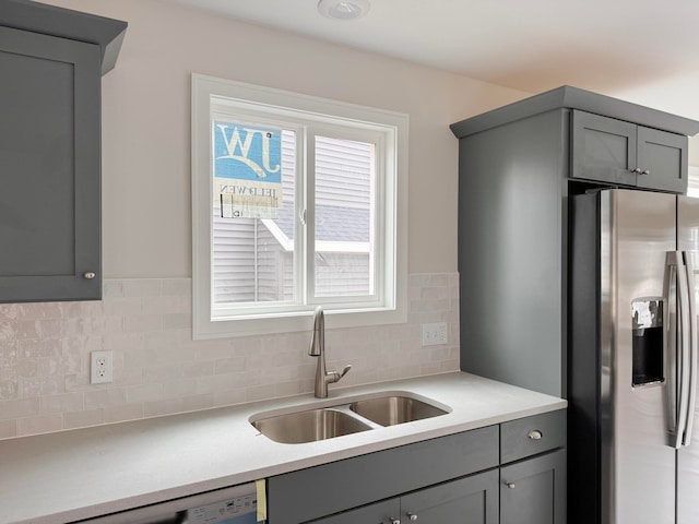 kitchen with stainless steel refrigerator with ice dispenser, sink, tasteful backsplash, and gray cabinetry