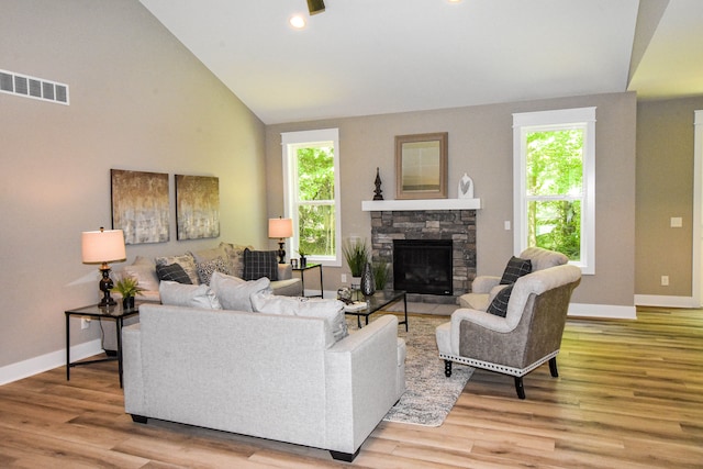 living room featuring a stone fireplace, hardwood / wood-style floors, a healthy amount of sunlight, and vaulted ceiling