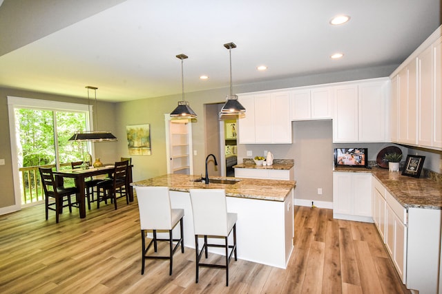 kitchen featuring light wood-type flooring, a kitchen island with sink, sink, decorative light fixtures, and white cabinets