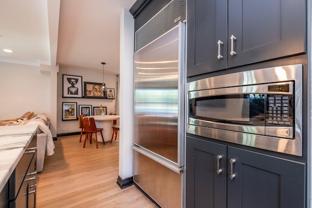 kitchen featuring pendant lighting, built in appliances, light hardwood / wood-style floors, and blue cabinets