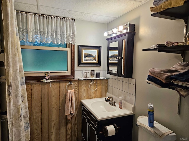 bathroom with a paneled ceiling, decorative backsplash, toilet, and vanity