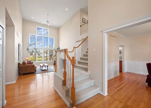 staircase with wood-type flooring, a towering ceiling, ceiling fan, and crown molding