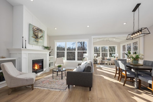 living room with a wealth of natural light, ceiling fan, vaulted ceiling, and light wood-type flooring