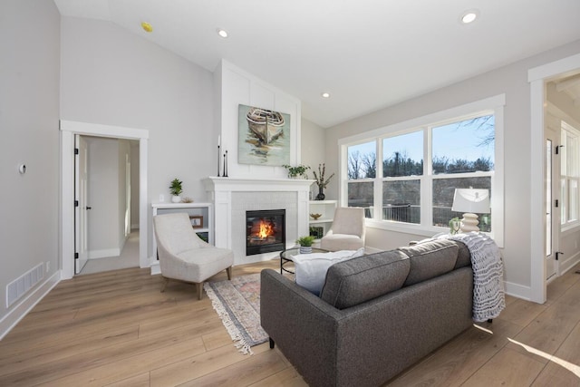 living room with light wood-type flooring, a tiled fireplace, and vaulted ceiling