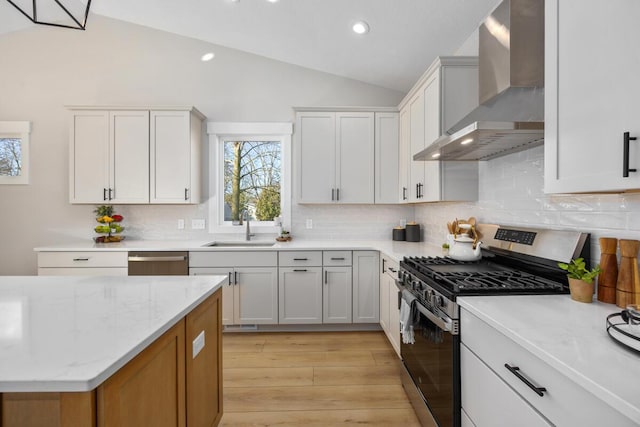 kitchen with appliances with stainless steel finishes, wall chimney exhaust hood, vaulted ceiling, sink, and white cabinets