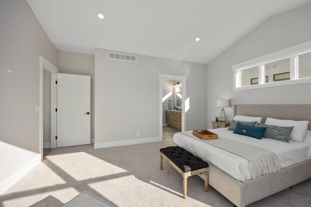 bedroom with ensuite bathroom, light colored carpet, and lofted ceiling