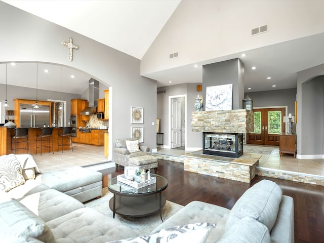 living room featuring light hardwood / wood-style floors, a fireplace, high vaulted ceiling, and french doors