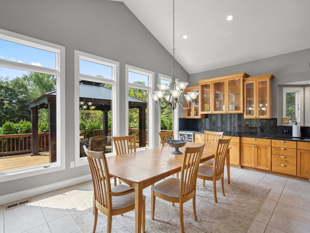 tiled dining space featuring high vaulted ceiling, a healthy amount of sunlight, and an inviting chandelier