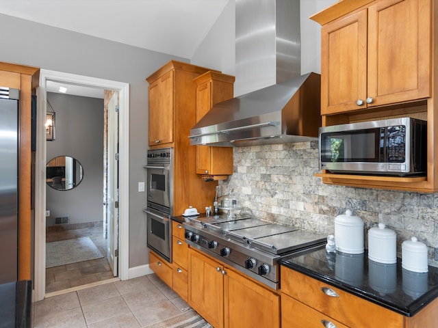 kitchen featuring backsplash, wall chimney exhaust hood, dark stone countertops, light tile patterned floors, and appliances with stainless steel finishes