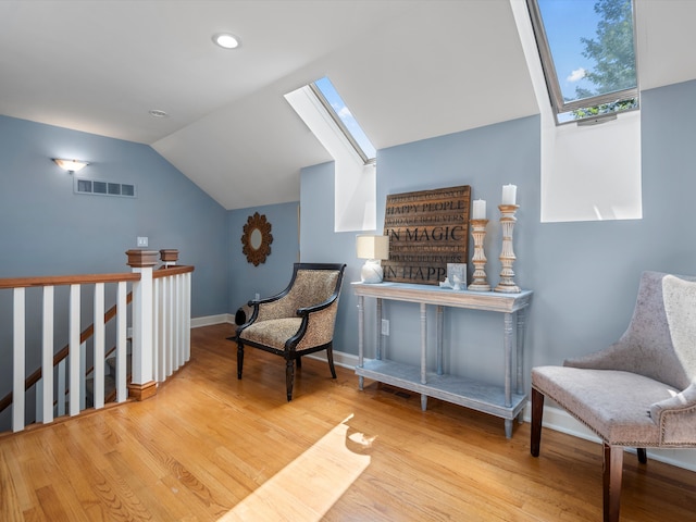 living area featuring vaulted ceiling with skylight and light hardwood / wood-style floors