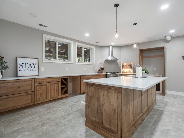 kitchen featuring high end stainless steel range oven, sink, wall chimney range hood, decorative light fixtures, and a center island with sink