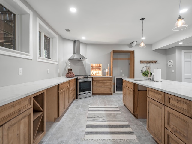 kitchen with light stone countertops, wall chimney exhaust hood, sink, decorative light fixtures, and stainless steel range with gas stovetop