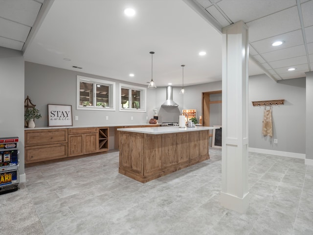 kitchen featuring a drop ceiling, wall chimney exhaust hood, light tile patterned floors, a center island, and hanging light fixtures