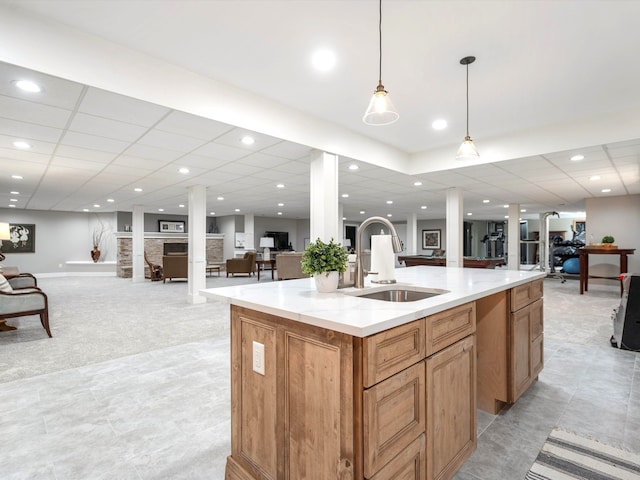 kitchen with a paneled ceiling, a center island with sink, sink, decorative light fixtures, and light colored carpet