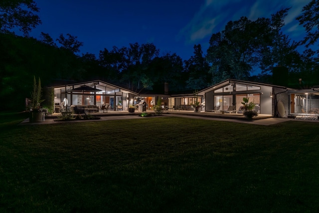 back house at twilight featuring a lawn