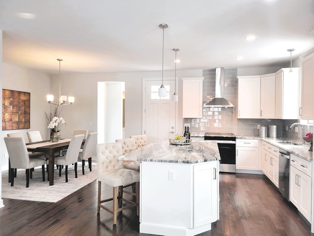 kitchen featuring decorative light fixtures, a center island, stainless steel appliances, and wall chimney range hood