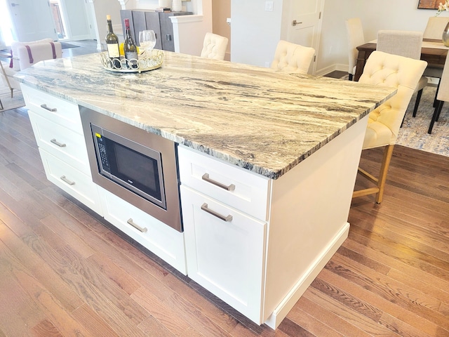 kitchen featuring white cabinetry, stainless steel microwave, wood-type flooring, and light stone counters