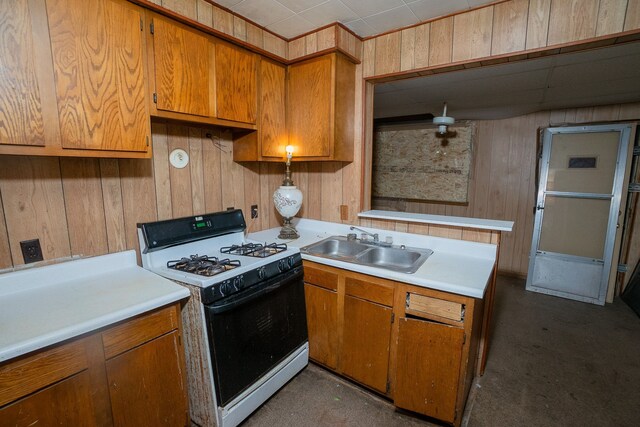 kitchen featuring white range with gas stovetop, sink, and wooden walls