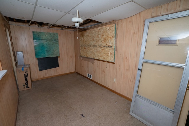 unfurnished room with a drop ceiling, wood walls, and light carpet