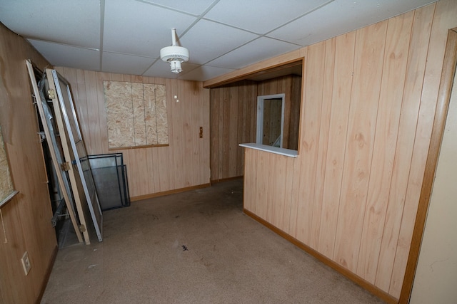 basement featuring a paneled ceiling, wood walls, and light colored carpet