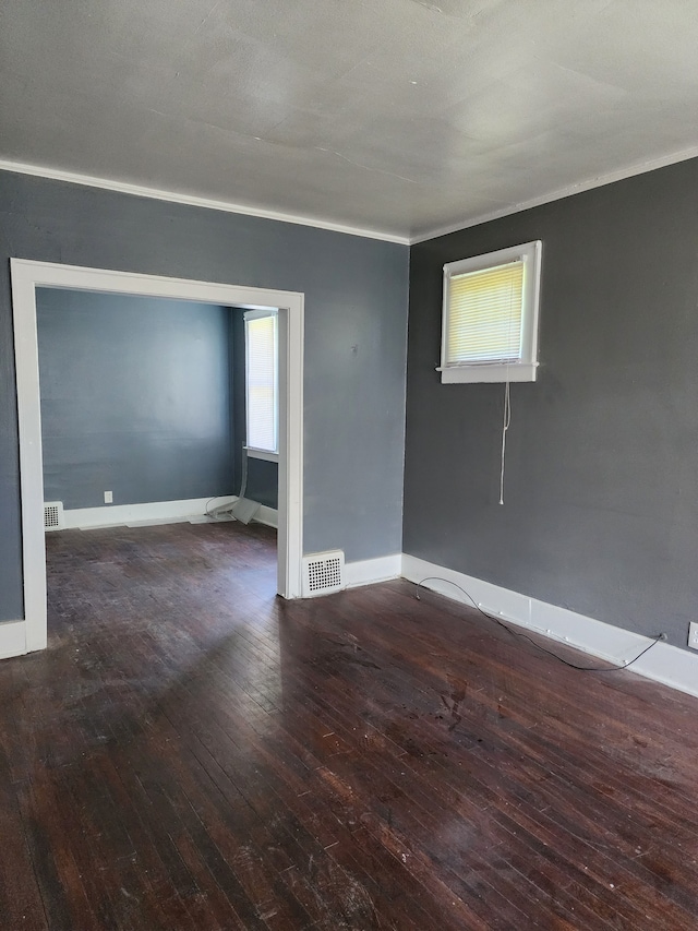 empty room featuring a wealth of natural light, dark hardwood / wood-style flooring, and crown molding