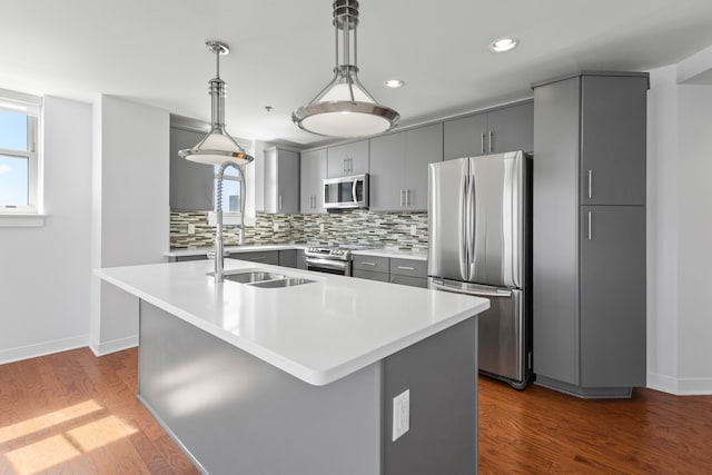 kitchen with gray cabinets, decorative light fixtures, stainless steel appliances, a healthy amount of sunlight, and a center island with sink