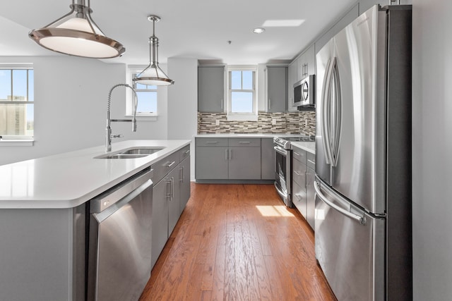 kitchen featuring gray cabinets, decorative light fixtures, sink, a kitchen island with sink, and stainless steel appliances