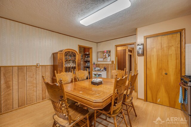 4100 Grass Lake Rd, West Branch, MI 48661 - dining room featuring a textured ceiling, light wood-style floors, a wainscoted wall, and wood walls