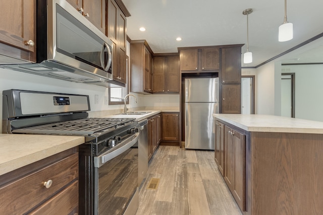 kitchen featuring sink, light hardwood / wood-style flooring, ornamental molding, appliances with stainless steel finishes, and decorative light fixtures