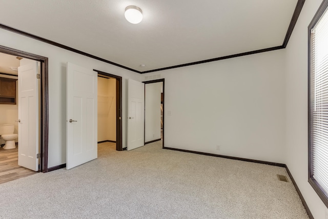 unfurnished bedroom featuring multiple windows, ensuite bathroom, and light colored carpet