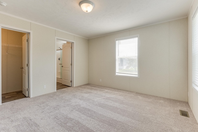 575 Gallery Dr Unit 48, Eaton Rapids, MI 48827 - unfurnished bedroom with carpet floors, ornamental molding, a spacious closet, a textured ceiling, and connected bathroom