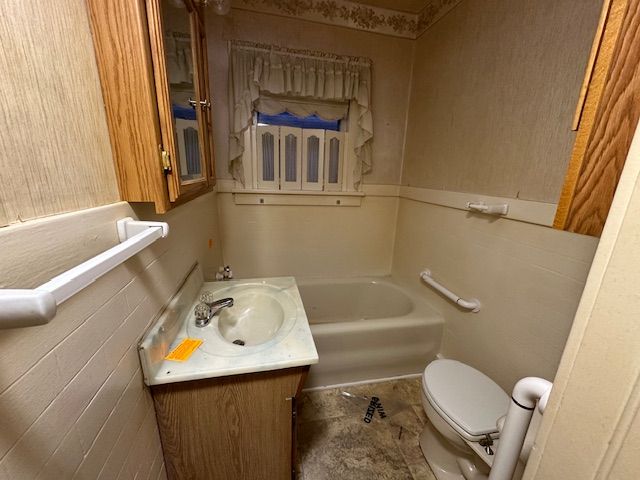 bathroom with vanity, toilet, a tub to relax in, and tile walls