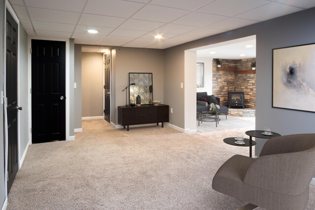 sitting room featuring light carpet, a paneled ceiling, and a wood stove