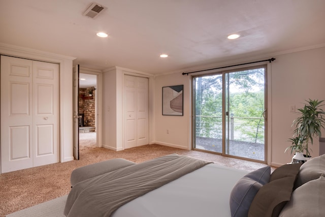 carpeted bedroom with a large fireplace, crown molding, and two closets