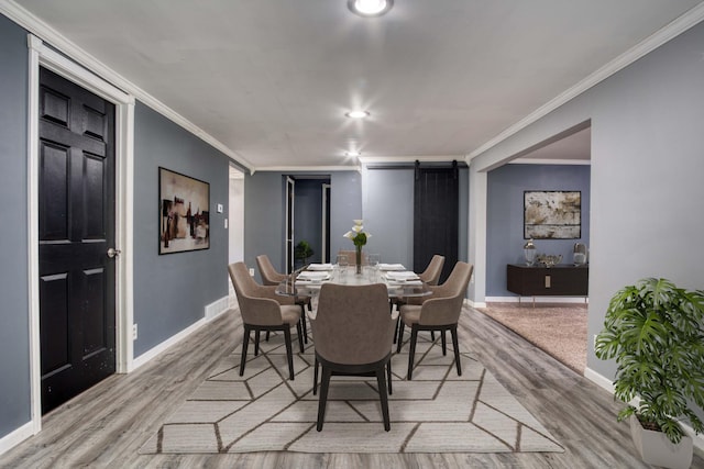 dining room featuring a barn door, light wood-type flooring, and crown molding