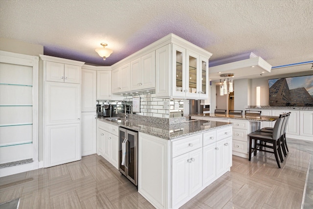 kitchen featuring white cabinets, kitchen peninsula, beverage cooler, and dark stone counters