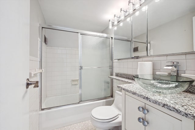 full bathroom with tile patterned floors, bath / shower combo with glass door, vanity, tile walls, and toilet