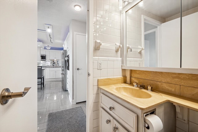 bathroom featuring decorative backsplash, tile patterned floors, vanity, a textured ceiling, and tile walls