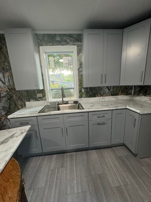 kitchen featuring light stone countertops, sink, tasteful backsplash, light hardwood / wood-style flooring, and gray cabinets