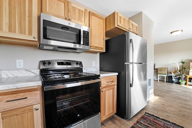 kitchen with appliances with stainless steel finishes, light hardwood / wood-style floors, and light brown cabinetry