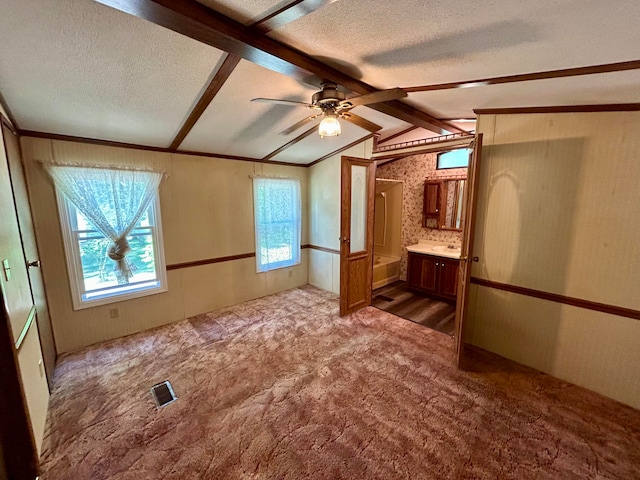 unfurnished bedroom featuring connected bathroom, a textured ceiling, carpet floors, ceiling fan, and vaulted ceiling with beams