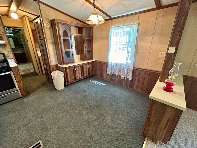 kitchen featuring wooden walls, stainless steel range oven, decorative light fixtures, and dark colored carpet