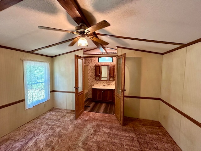 interior space with ceiling fan, sink, lofted ceiling with beams, a textured ceiling, and carpet