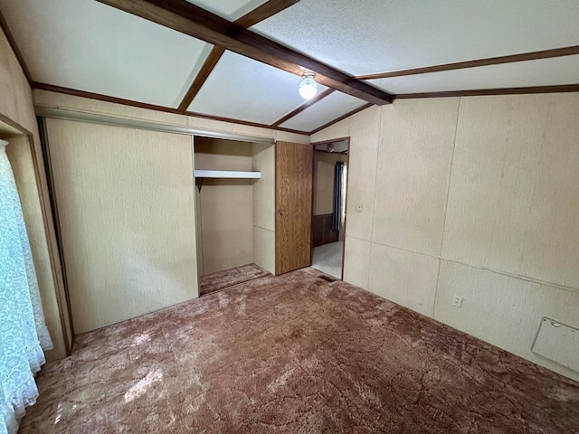 unfurnished bedroom with carpet, lofted ceiling with beams, and a closet