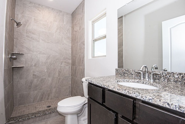 bathroom featuring tile patterned flooring, a tile shower, vanity, and toilet