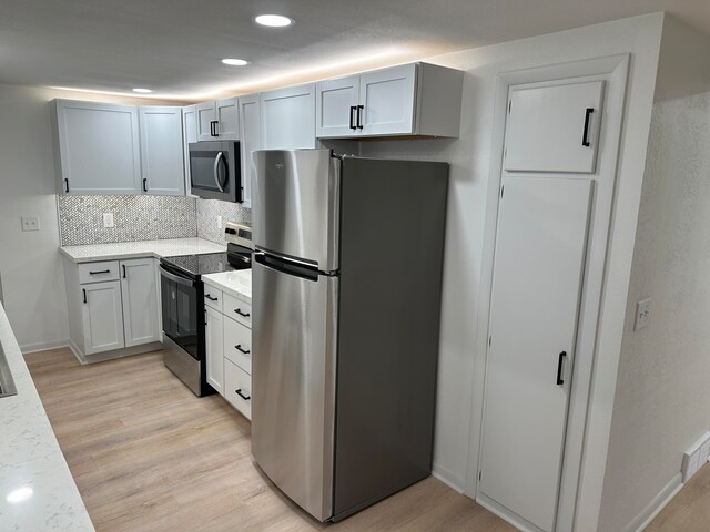 kitchen with light hardwood / wood-style flooring, light stone countertops, appliances with stainless steel finishes, tasteful backsplash, and white cabinetry