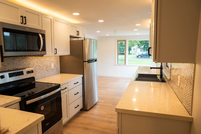 kitchen with light stone countertops, sink, stainless steel appliances, light hardwood / wood-style flooring, and white cabinets