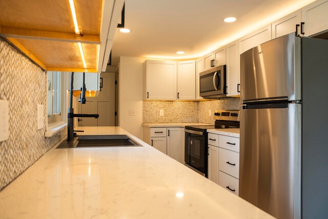 kitchen with light stone countertops, sink, tasteful backsplash, white cabinets, and appliances with stainless steel finishes