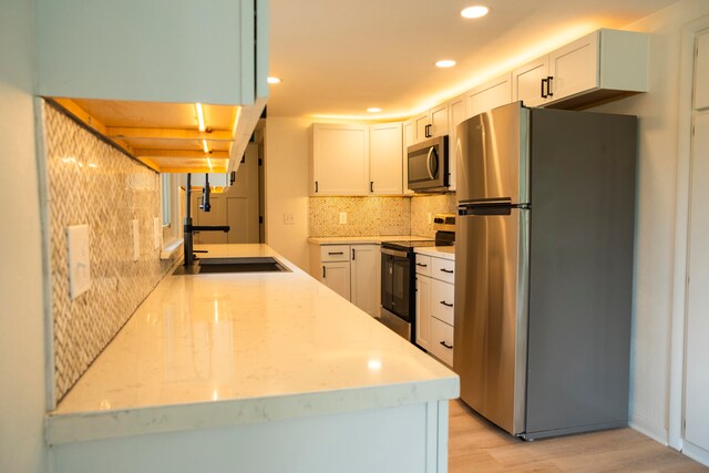 kitchen with appliances with stainless steel finishes, light wood-type flooring, and white cabinetry